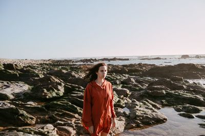 Portrait of young woman standing on rock by sea against clear sky