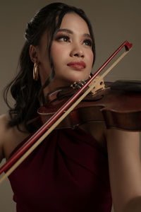 Young woman playing violin while standing against white background