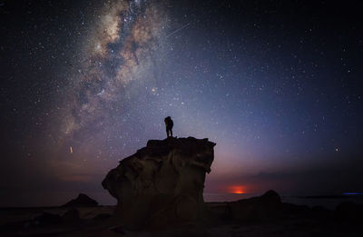 Silhouette man on rock formations against star field in sky at night