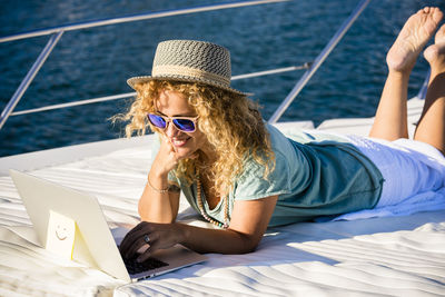 Smiling woman using laptop while lying down on boat deck