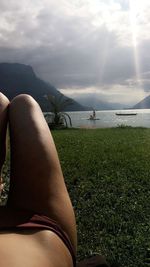 Low section of woman relaxing on grass by sea against sky