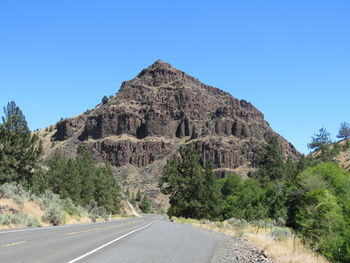 Road by mountain against clear blue sky