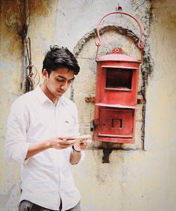 Young man using smart phone while standing against wall