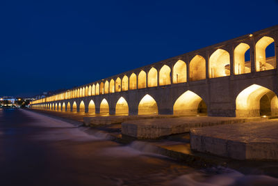 Arch bridge against clear blue sky at night