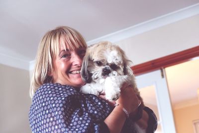 Portrait of smiling young woman holding dog at home