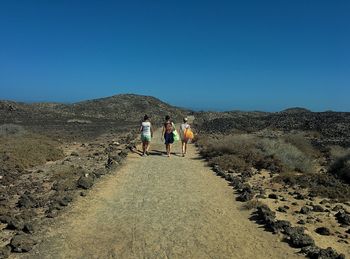 People walking on landscape against clear blue sky