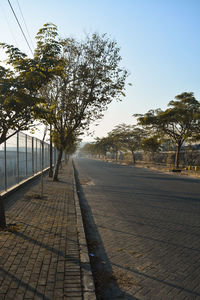 Empty road by trees against sky