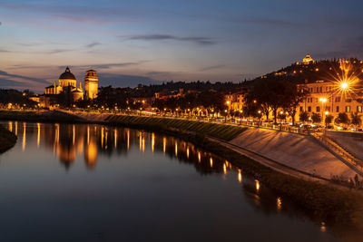 Illuminated buildings by river against sky at night