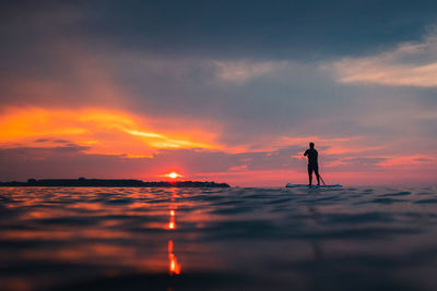 Silhouette man standing on paddleboard against sky during sunset