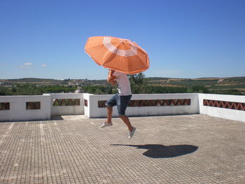 Young man with umbrella jumping on terrace during sunny day