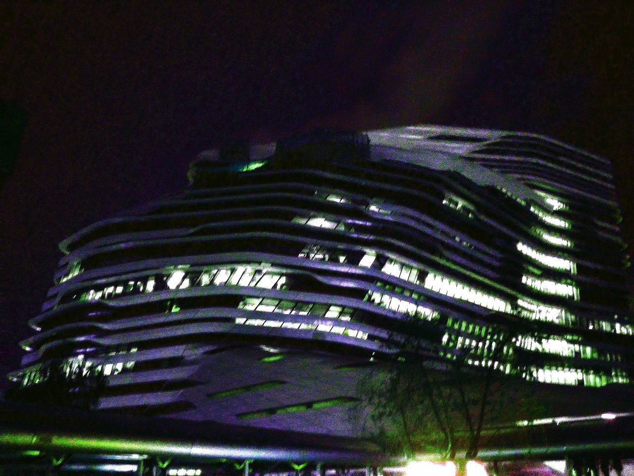 tree, low angle view, built structure, architecture, night, building exterior, growth, green color, illuminated, modern, building, outdoors, tall - high, no people, pattern, nature, sky, tree trunk, city