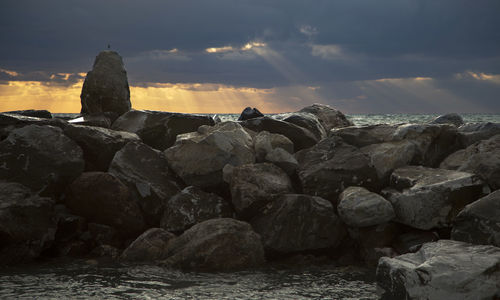 Rocks by sea against sky during sunset