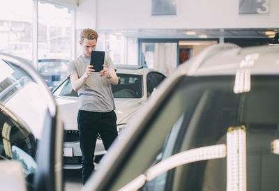 Man photographing car through digital tablet at dealership store