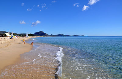 Playful child on shore at beach against blue sky