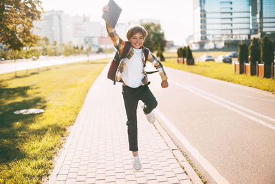 Full length of happy boy jumping on footpath