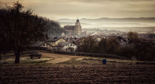 Houses on field by buildings against sky