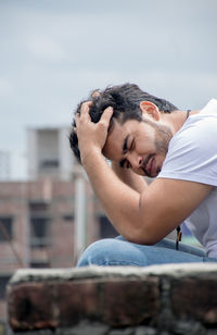 Young man with eyes closed sitting against building