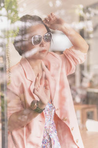 Woman wearing sunglasses seen through window