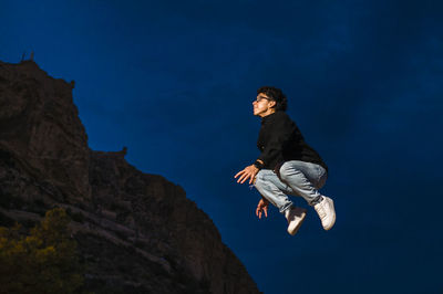 Young transgender man jumping outdoors at night.