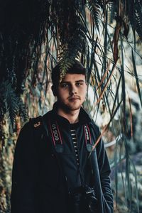 Portrait of young man standing against trees in forest