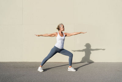 Woman doing warrior 2 pose in front of wall