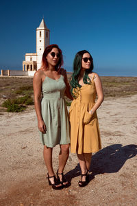 Two young women are posing in dresses in the desert with a church in the background. fashion concept