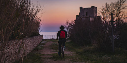 Rear view of man standing by bare trees against sky