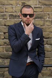 Portrait of businessman with hand on chin standing against brick wall