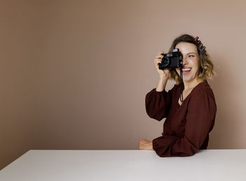 Young woman photographing while standing against wall