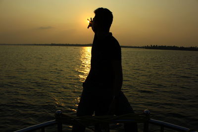 Rear view of woman on sea against sunset sky