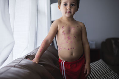 Cute shirtless boy standing on sofa at home