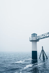 Lighthouse by sea against clear sky