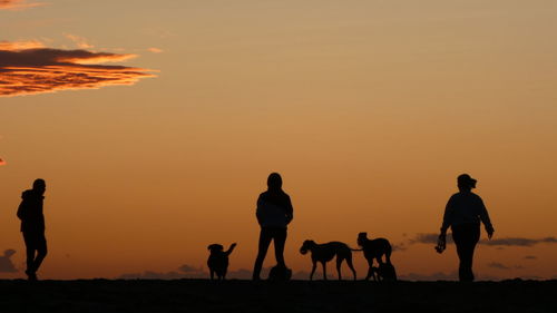 Silhouette people walking by sea against orange sky