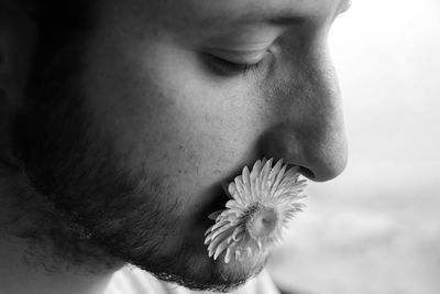 Close-up of man with flower in mouth against blurred background