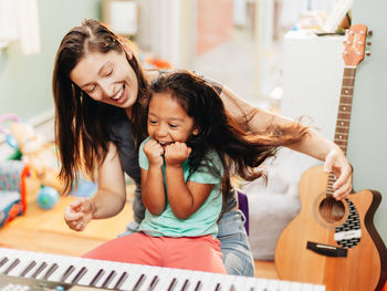 Happy mother teaching piano to daughter at home