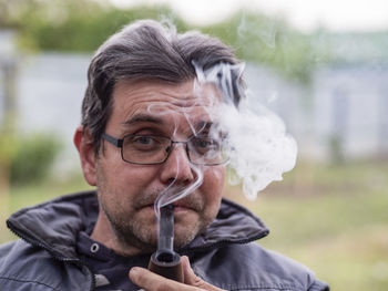 Unshaven caucasian man in glasses smokes a pipe