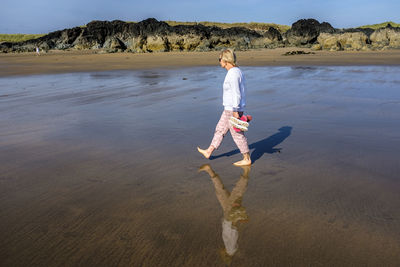 A blond woman walking alone and barefoot in the surf on a sunny day at rhosneigr beach, anglesey, uk