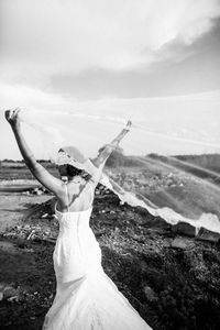 Rear view of bride holding veil on field against sky