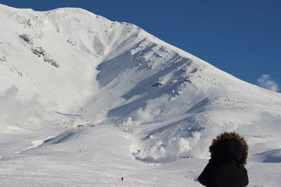 Rear view of woman sitting on snowcapped mountain against sky