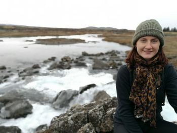 Portrait of smiling young woman standing at beach during winter