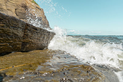 Waves splashing on rocks at shore against clear sky