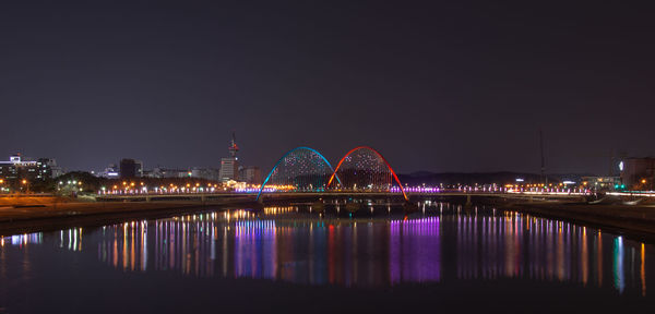 Illuminated bridge over river against sky at night