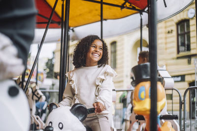 Happy girl looking away while enjoying ride on carousel during carnival at amusement park