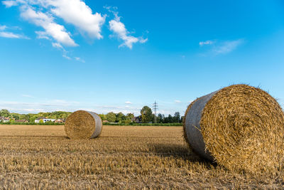 Hay bales on field against blue sky