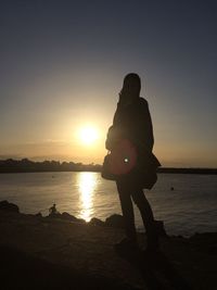 Silhouette woman standing on pier by lake against sky during sunset