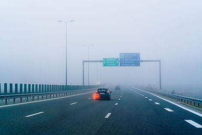 Vehicles on highway against sky in city in a foggy autumn morning