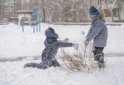 Two boys wear warm clothes are playing snowballs outdoor.