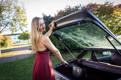 Portrait of young woman removing purse from car trunk