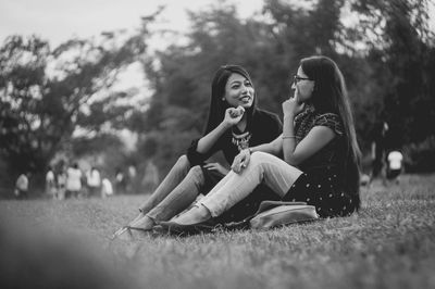 Young women sitting on grass against trees