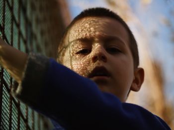 Close-up portrait of boy by fence